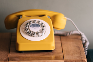 Telefone amarelo com fio em cima de uma superfície de madeira.