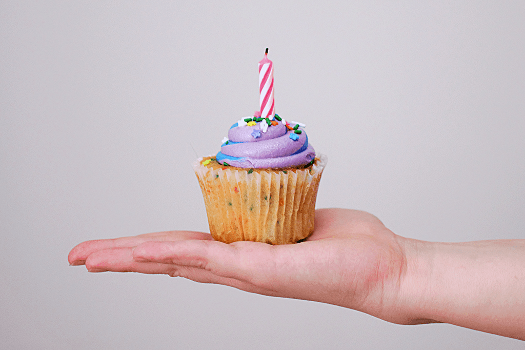 Uma mão segurando um cupcake com uma velinha de aniversário.