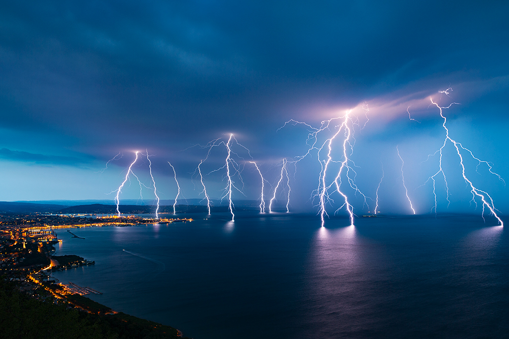 Foto de diversos raios caindo sobre cidade costeira e mar.