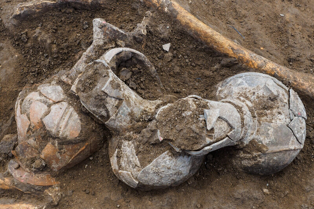Escavação mostrando esqueleto e cerâmicas encontrados.