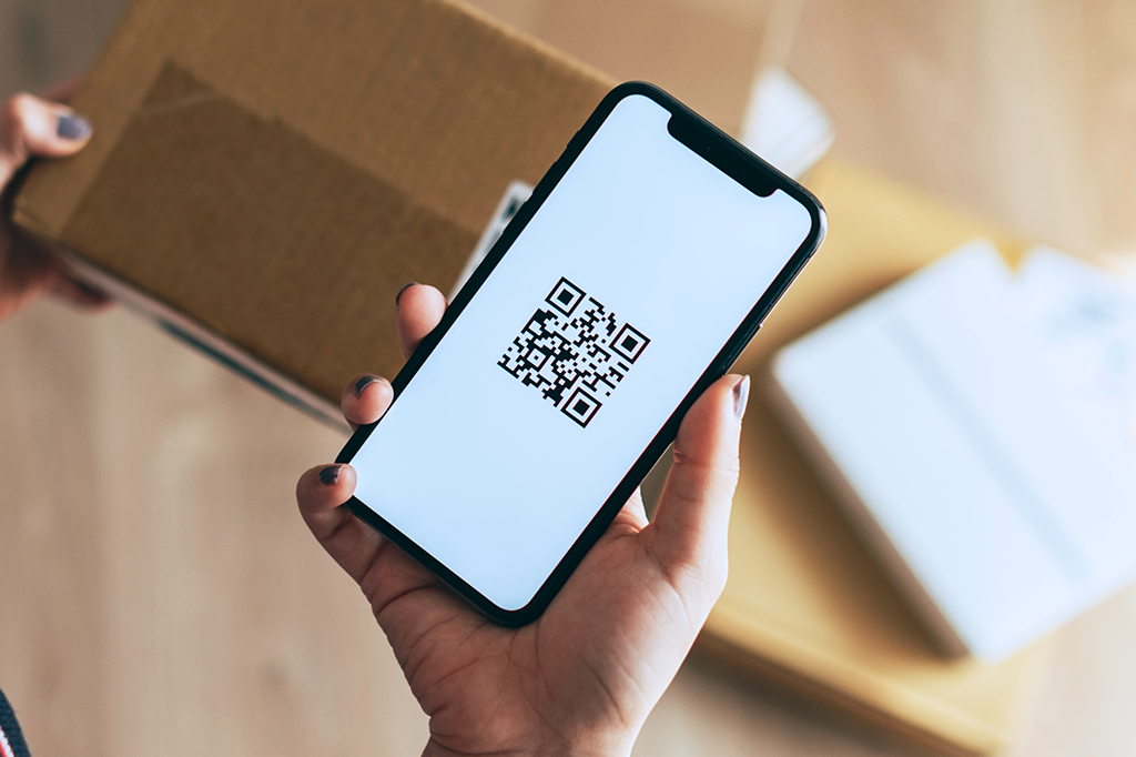 Foto de uma mulher segurando um celular com a imagem de um QR Code na tela.