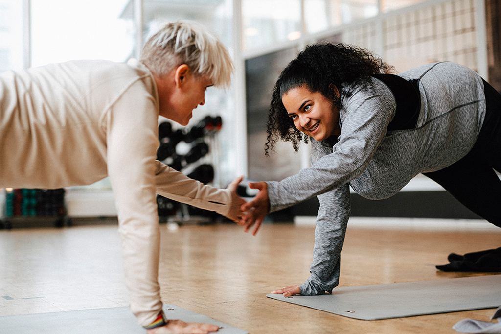 Duas mulheres batendo a mão uma a outra enquanto se exercitam.