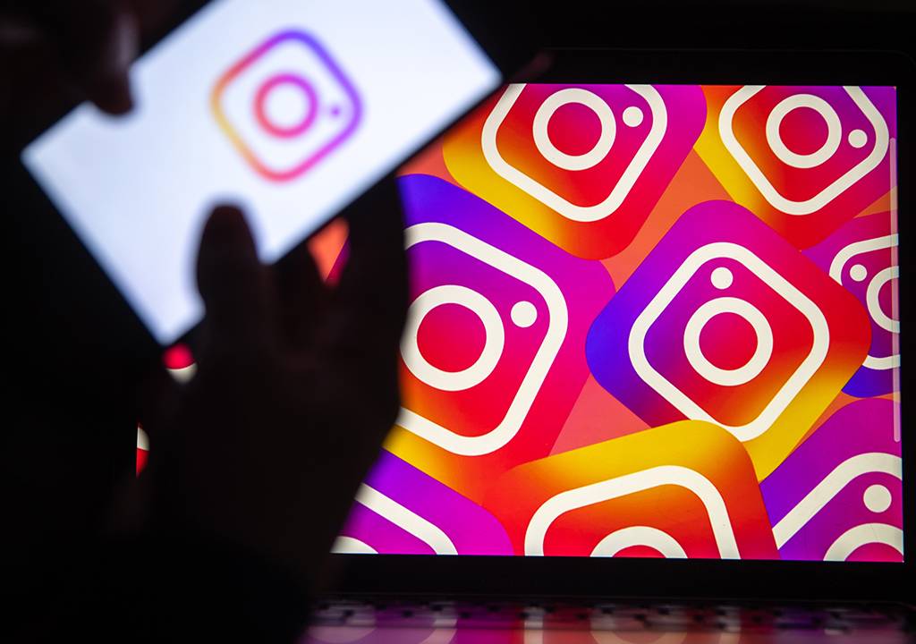 Logotipo do 'Instagram' exibido na tela de um telefone celular em frente à tela de um computador.