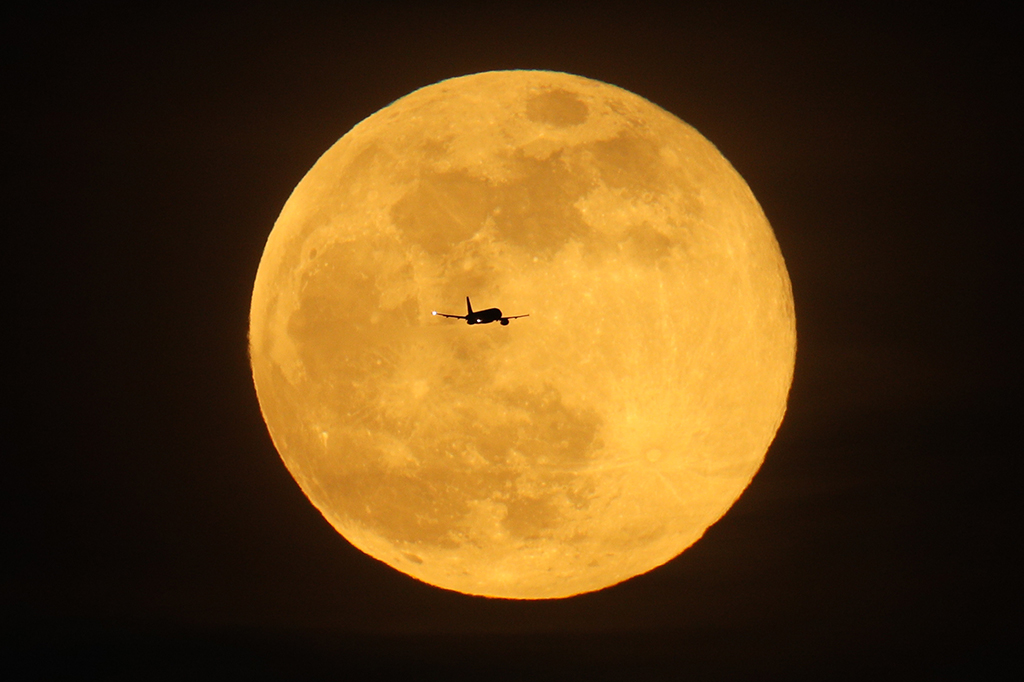 Um avião sobrevoando em frente a Lua.