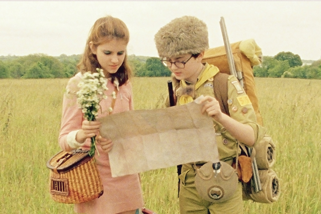 2709-Moonrise-Kingdom Duas crianças, lado a lado, no meio de um gramado. Elas estão segurando um mapa com as suas mãos.
