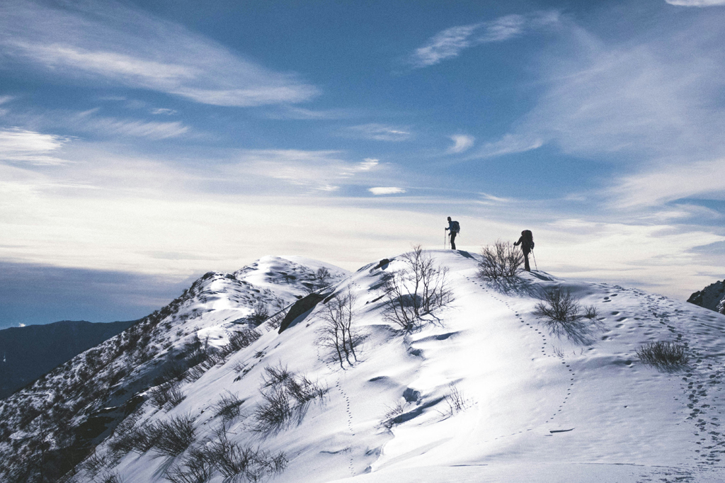 Imagem de dois alpinistas no cume de uma montanha nevada.