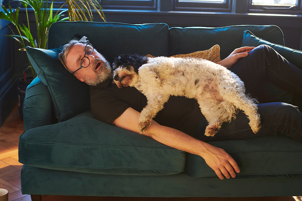 Foto de um senhor dormindo profundamente com o seu cachorro encima dele.