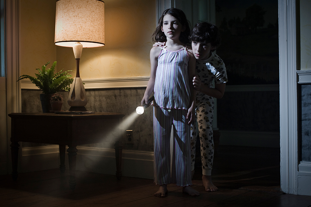 Fotografia de dois irmão, a menina está segurando a lanterna e o irmão se escondedo atrás dela.
