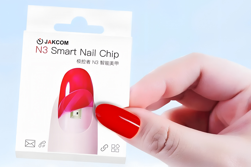 Imagem, em fundo azul claro, de uma m&atilde;o segurando, nas pontas dos dedos, uma embalagem de unha posti&ccedil;a que cont&eacute;m um chip.