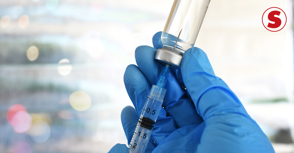 Fotografia de uma mão segurando uma seringa no frasco de vacina.