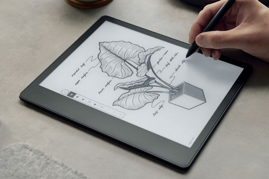 Imagem de uma m&atilde;o masculina segurando uma caneta &oacute;tica para Kindle. Na tela v&ecirc;-se um desenho de um vaso com uma planta de grande folhagem.