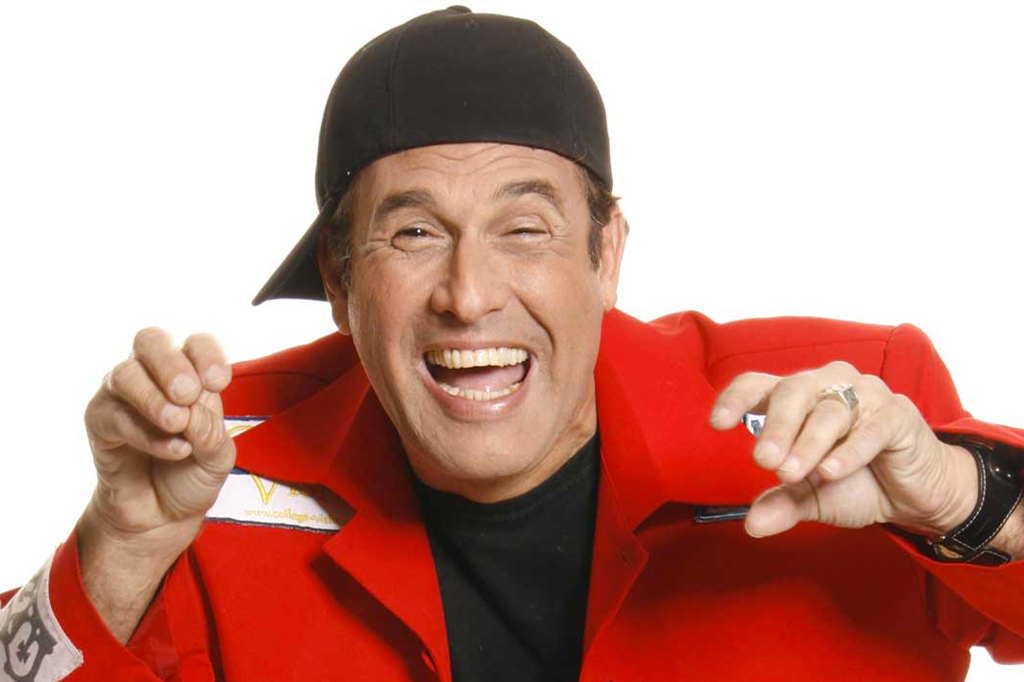 Imagem, em fundo branco, de um homem sorrindo, vestindo um terno vermelho e bon&eacute; preto.