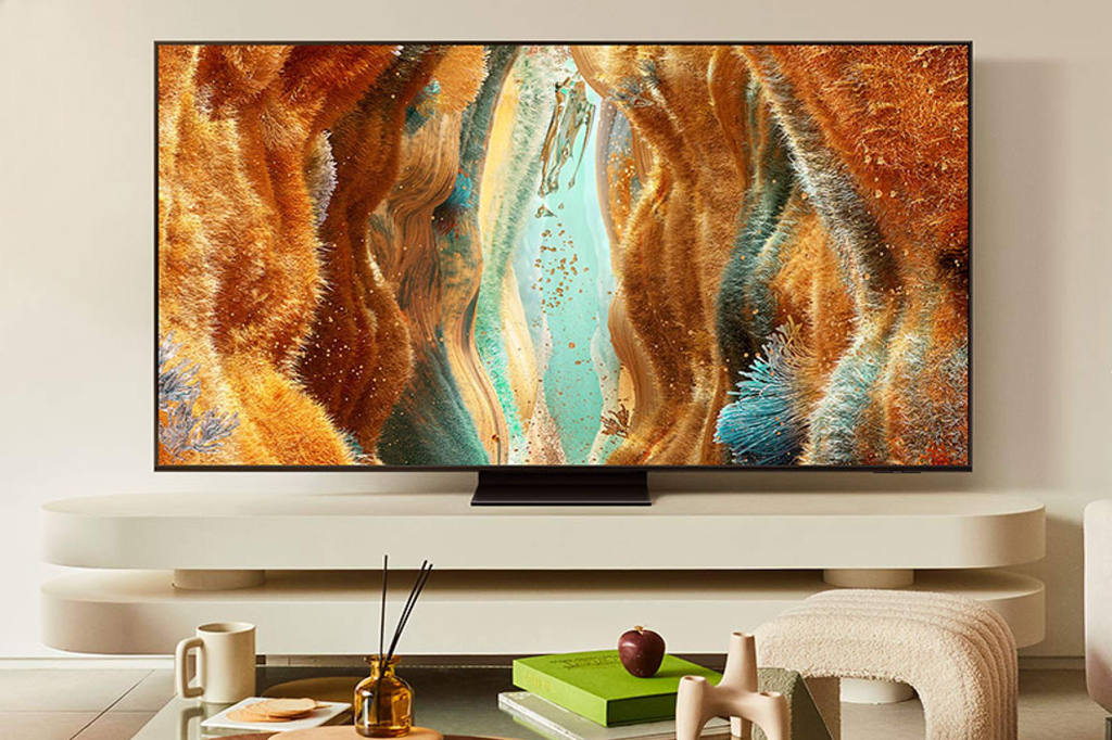 Imagem de uma grande Smart TV. Em primeiro plano, v&ecirc;-se alguns objetos de decora&ccedil;&atilde;o numa mesa de centro.