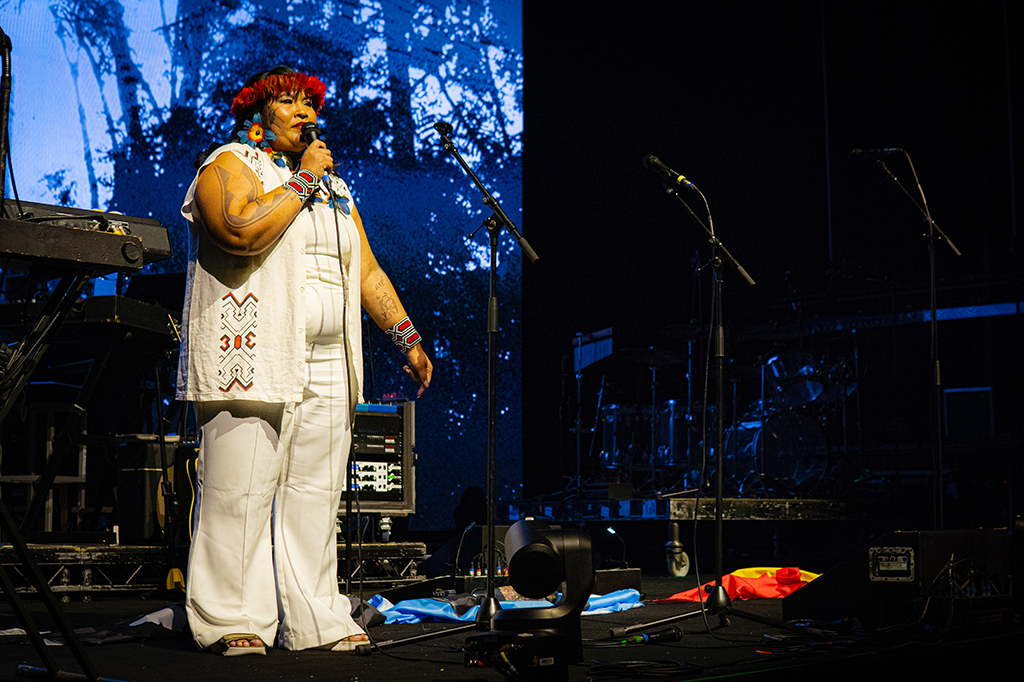 Fotografia do show do Massive Attack, Alana Manchineri discursa durante show do Massive Attack. Alana Manchineri discursando no palco.