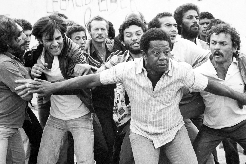 Imagem com cena do filme Eles N&atilde;o Usam Black-Tie (1981). V&ecirc;-se oper&aacute;rios exaltados reunidos durante uma greve.