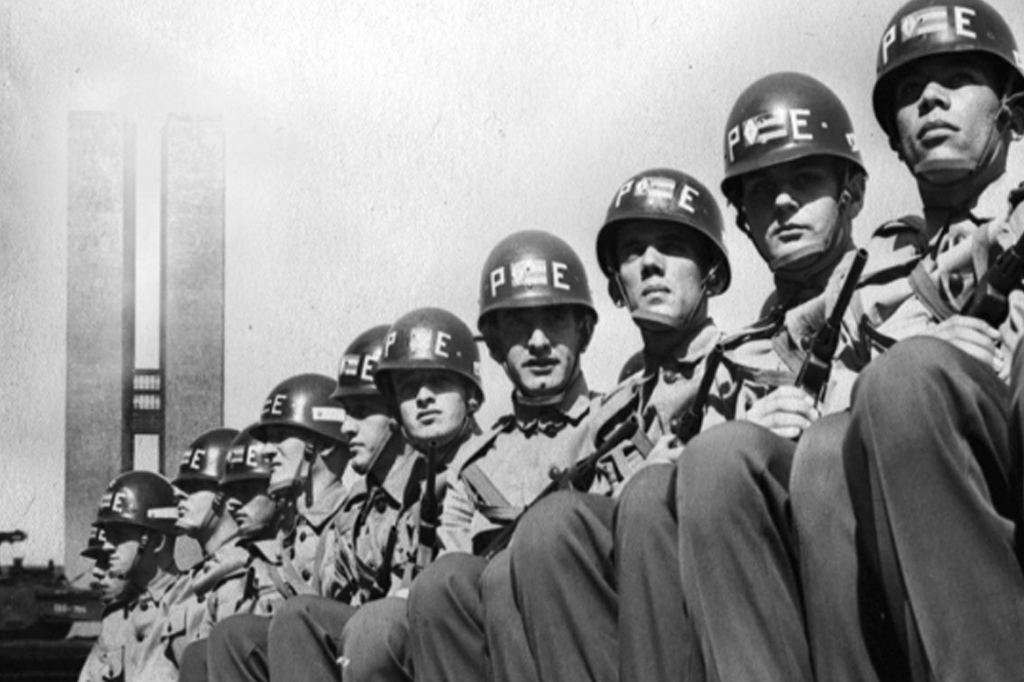 Imagem com cena do filme O Dia que Durou 21 Anos (2012). V&ecirc;-se um grupo de policiais do ex&eacute;rcito perfilados. Ao fundo, o pr&eacute;dio do Congresso Nacional.