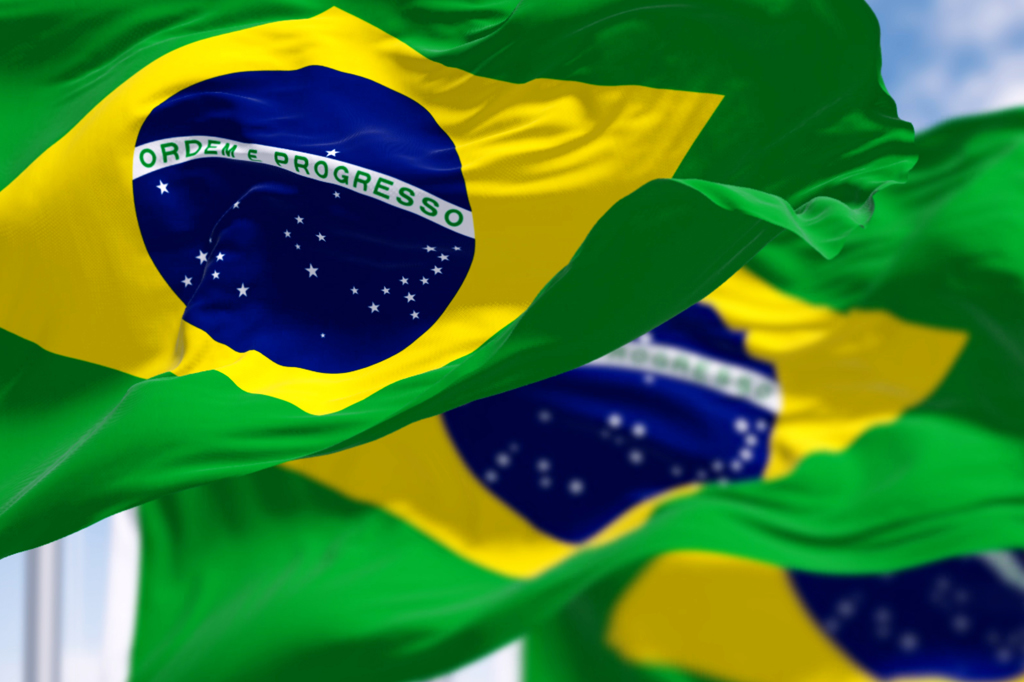 Imagem de três bandeiras do Brasil tremulando ao vento.
