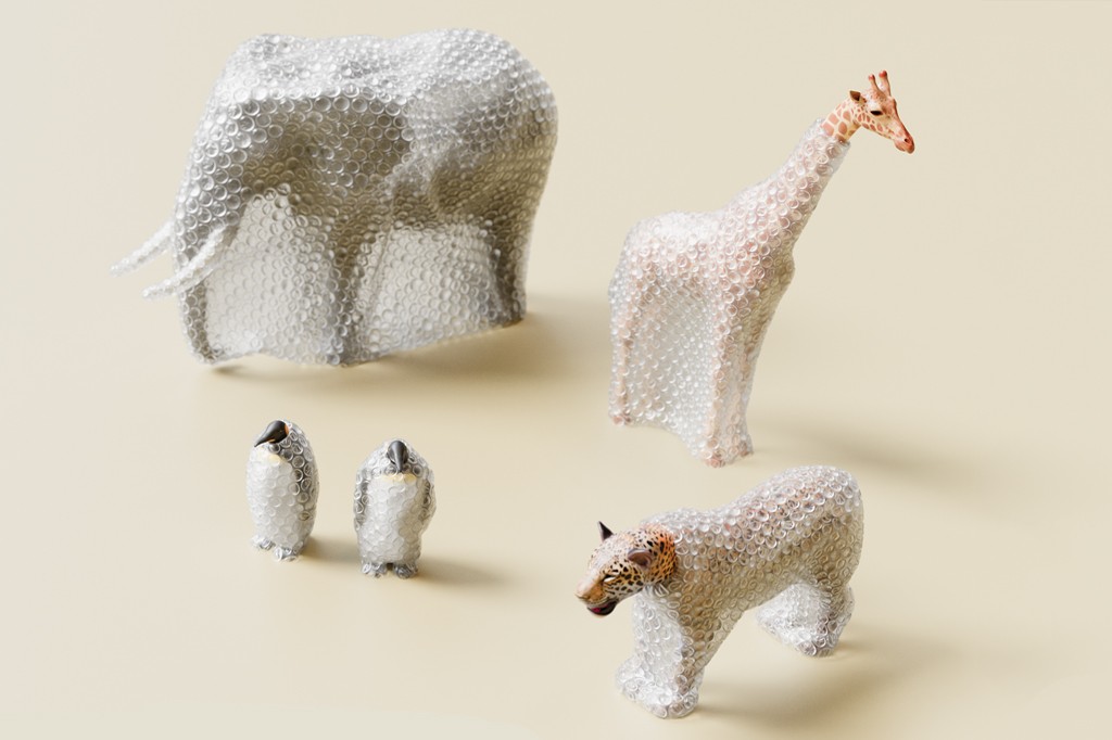 Estatuetas de animais embrulhadas em pl&aacute;stico bolha: um elefante, uma girafa, dois pinguins e um leopardo, com as cabe&ccedil;as e detalhes expostos, sobre um fundo bege claro.